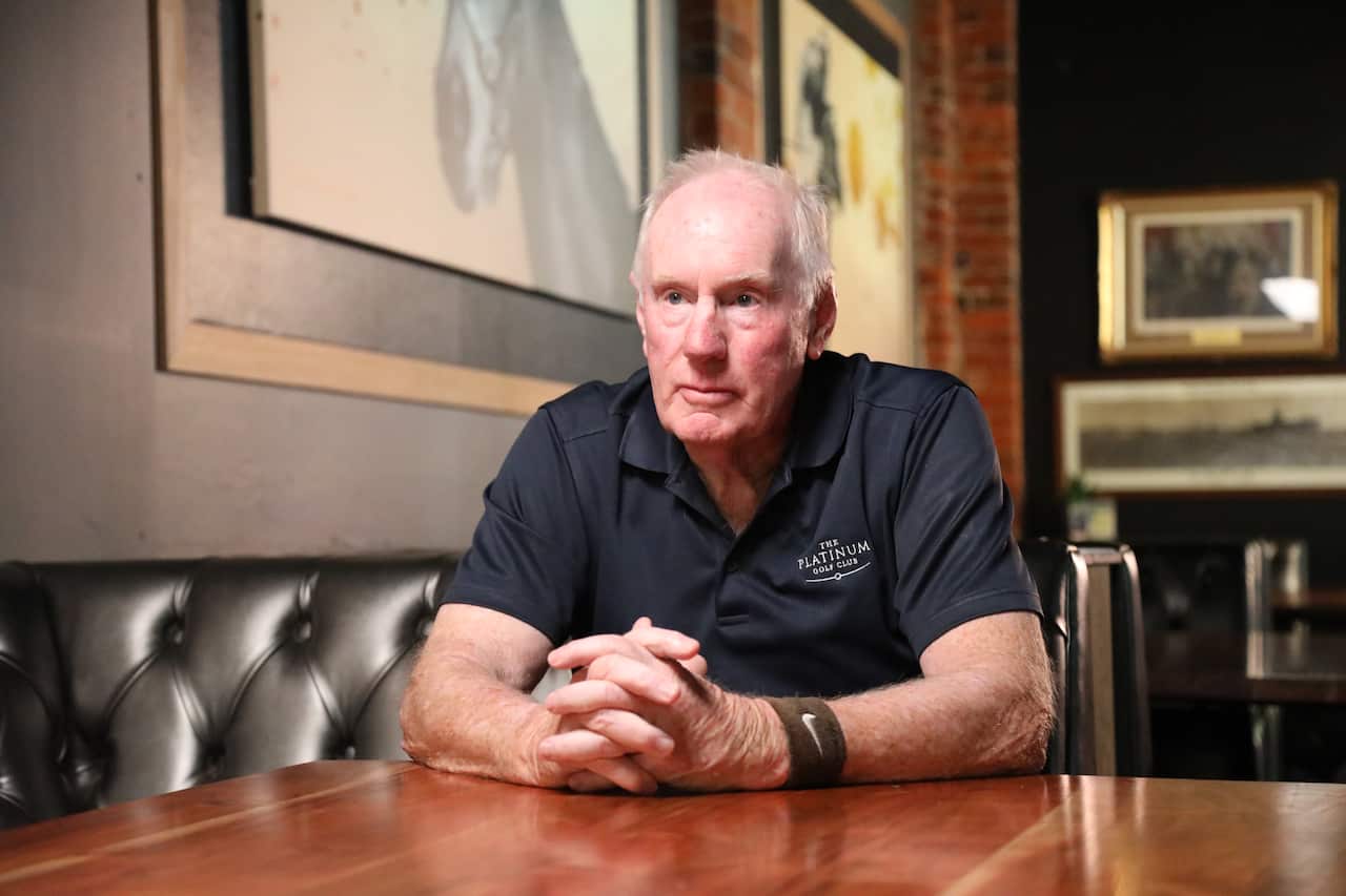 A man in a black polo shirt sits at a table.