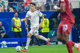 A footballer wearing a white shirt and white shorts runs down the field with the ball at his feet.