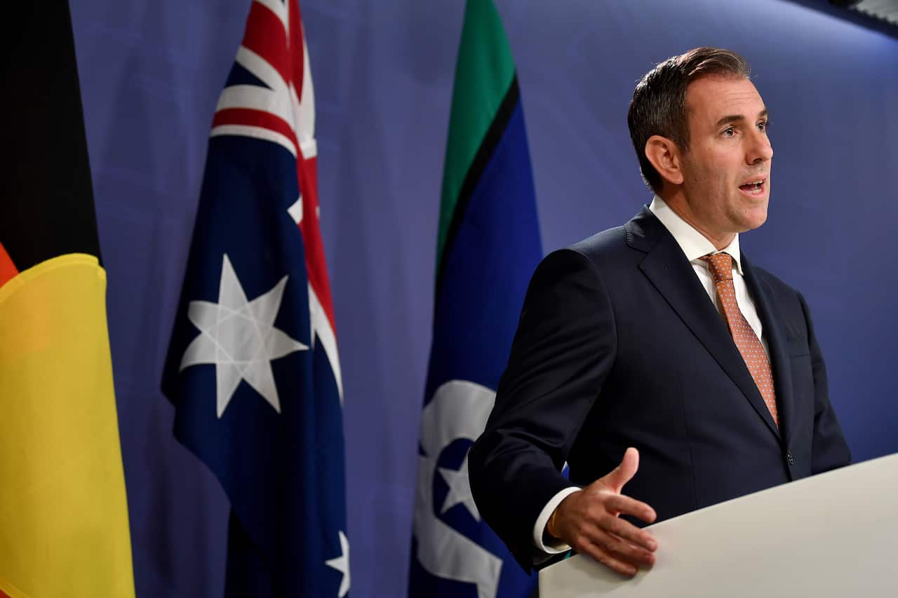 Man in suit in front of Australian and Indigenous flags.