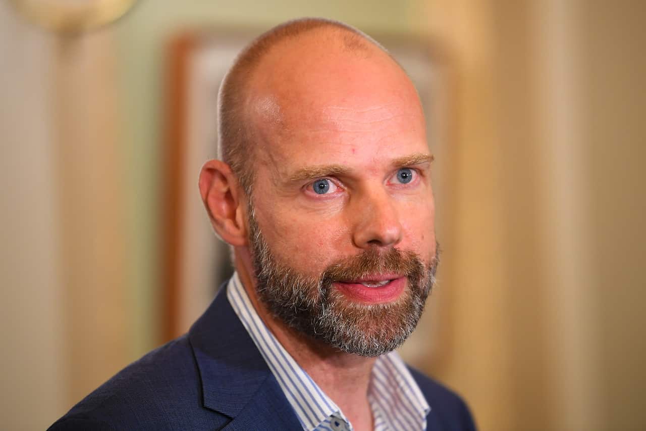 Jeroen is in a navy suit and unbuttoned shirt looking straight ahead.