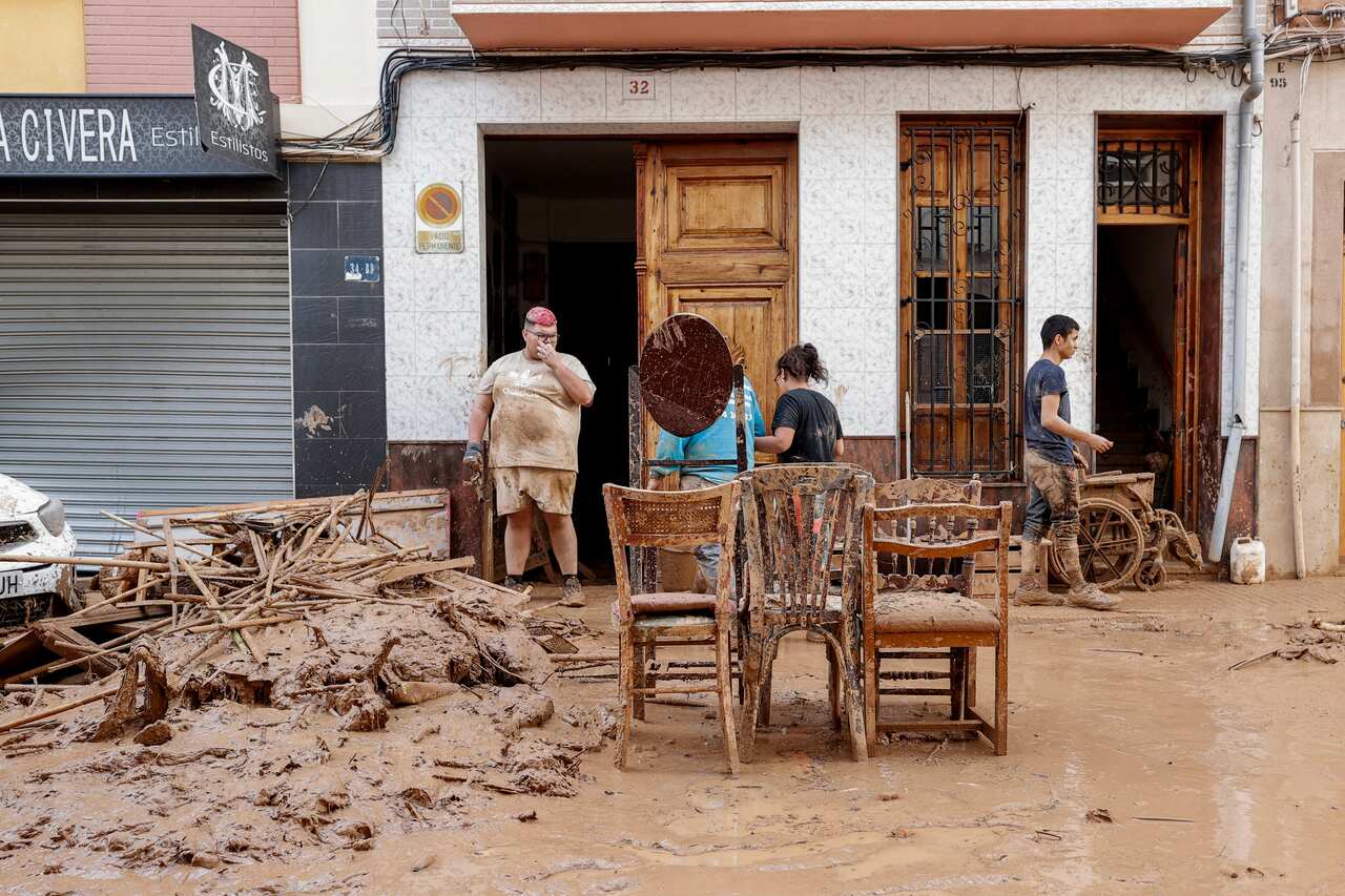 A group of people inspect muddied furniture on a street