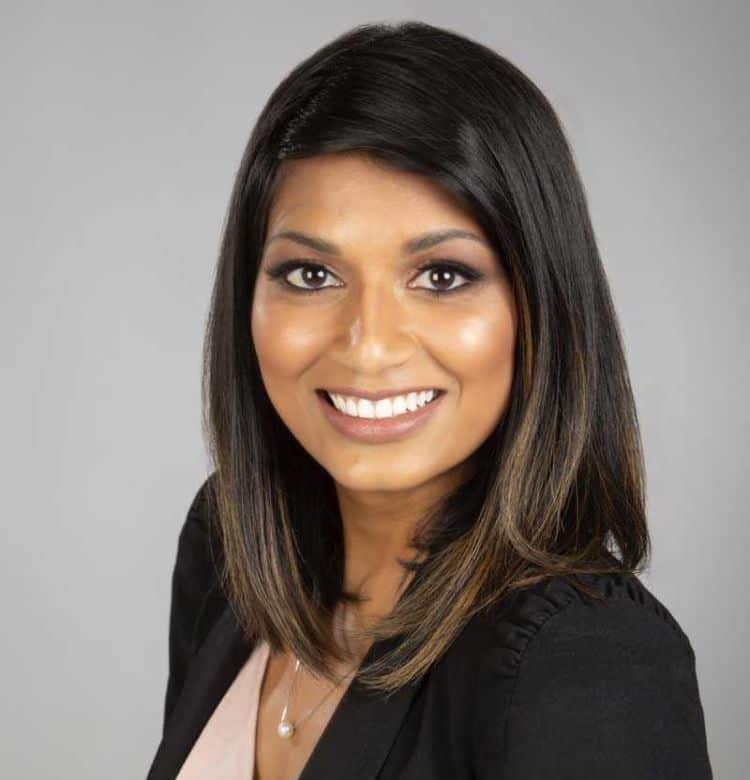 A south Asian woman wearing a black blazer and pale pink top smiles