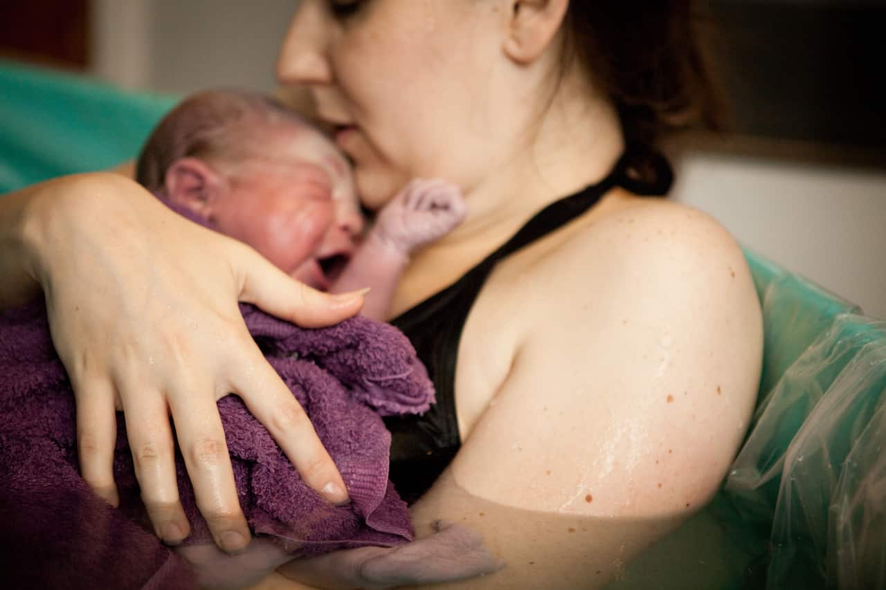 A mother holding her newborn baby in the water of a birthing tub