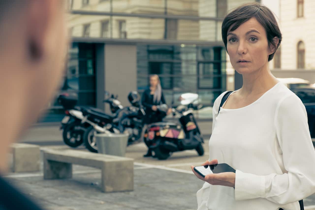A woman holding a phone looks curiously at a man off frame in Breaking Point