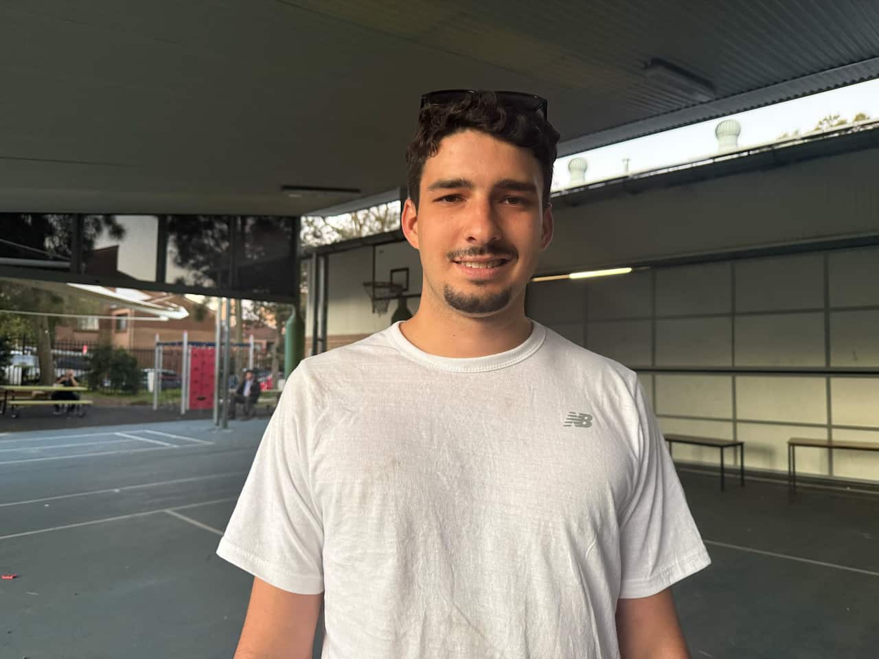 A man stands on a sports court in a white top.