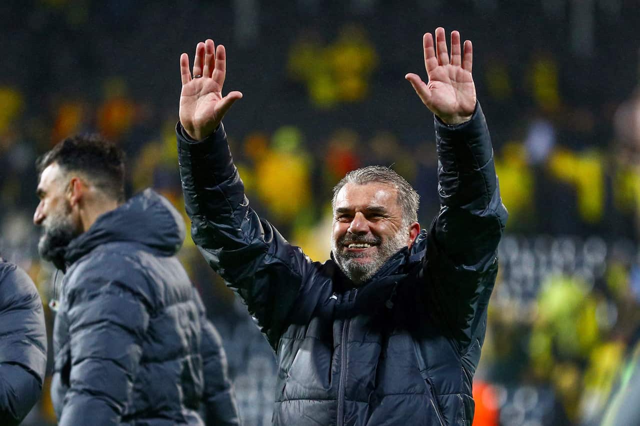 A man in a dark parka smiles and raises his hands above his head