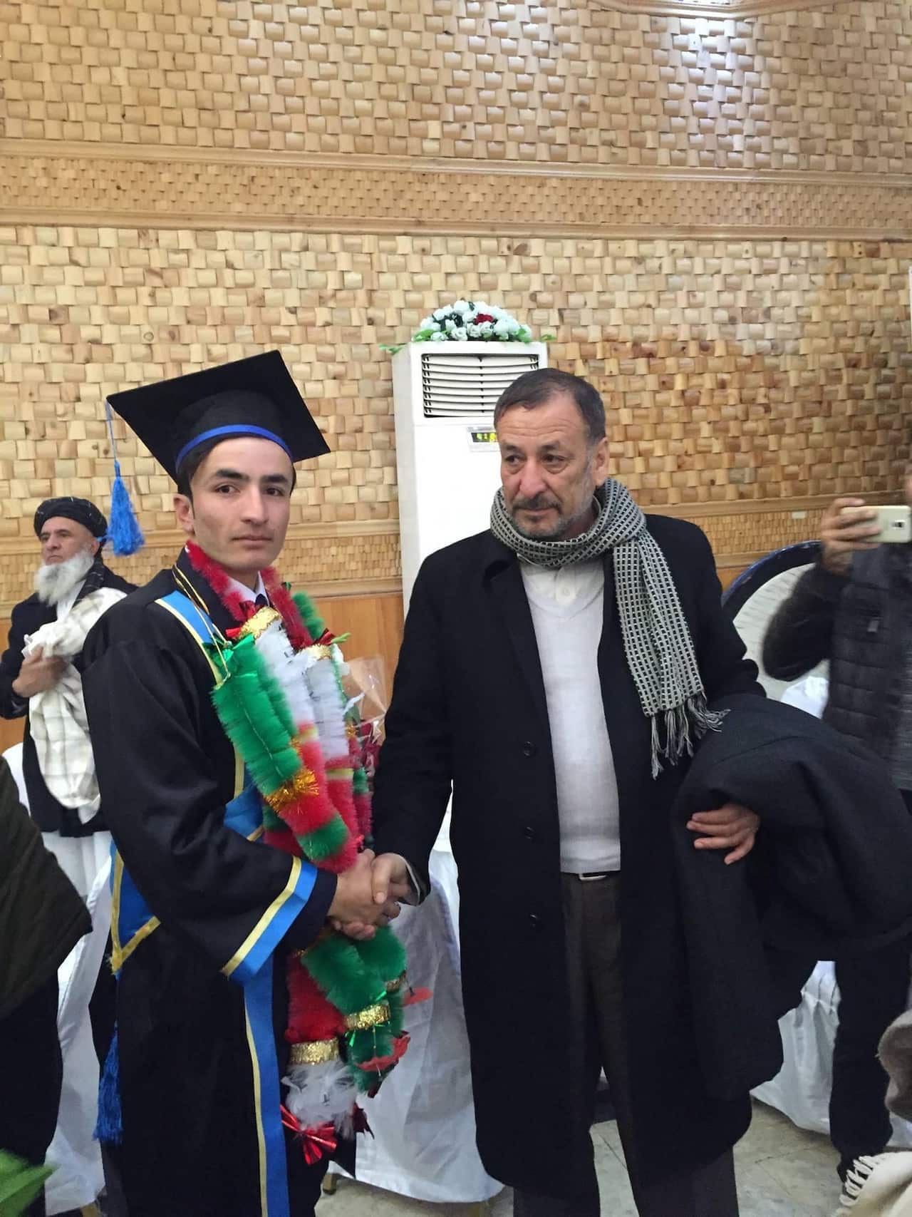 Tariq Zia, wearing a gown and mortar board, at his graduation ceremony, standing next to his father.