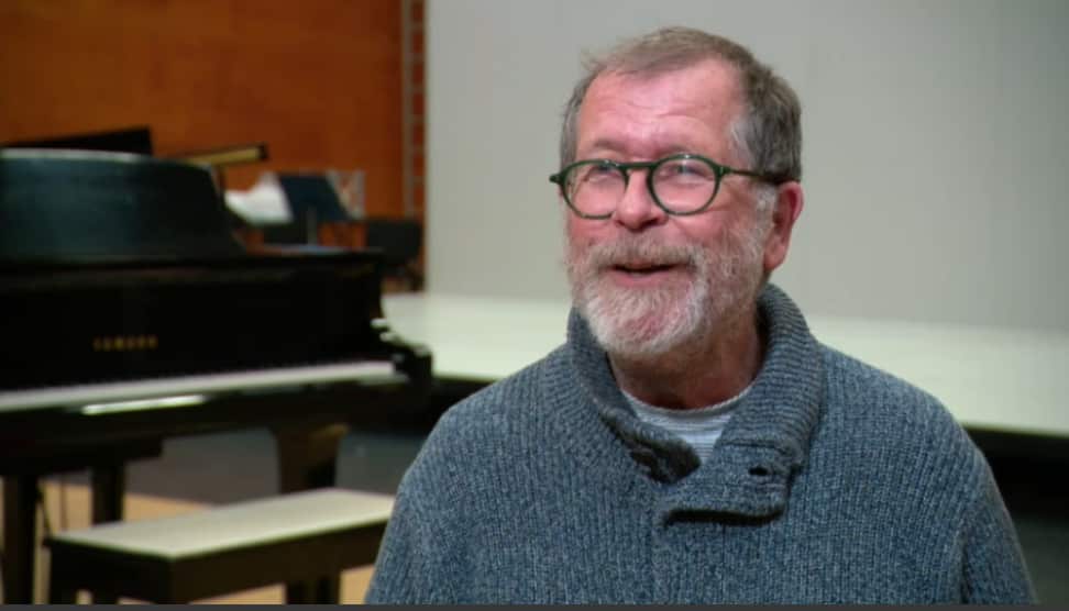 A man in a blue woollen jumper and green glasses