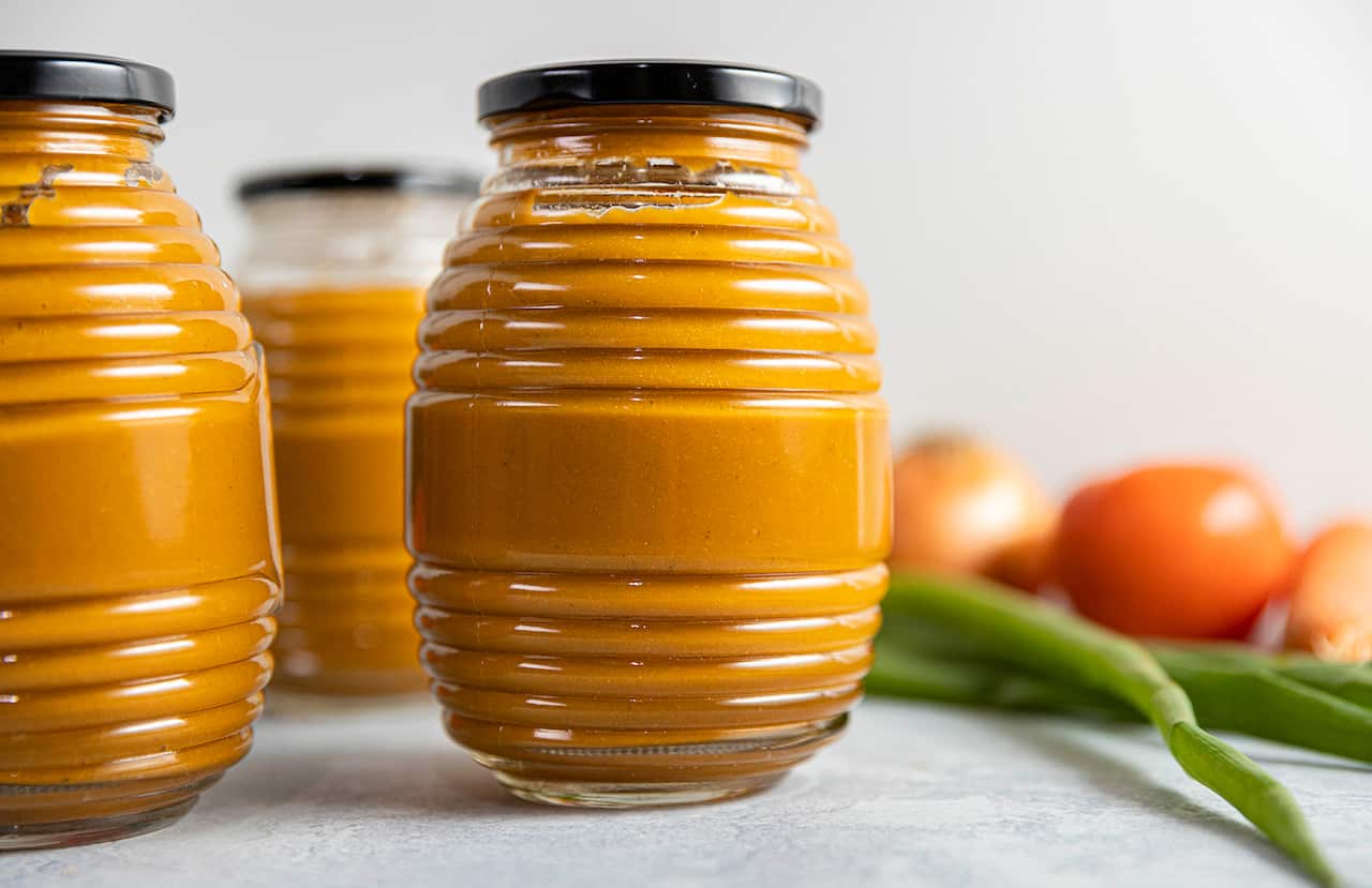 Three interesting glass jars with with a grooved pattern around the circumerence and black lids are filled with an orange sauce. 