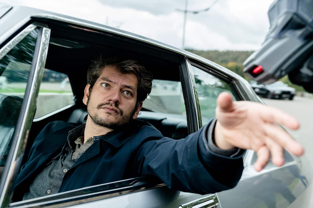 A man leans out of a car windown, holding his hand towards a scanner. 