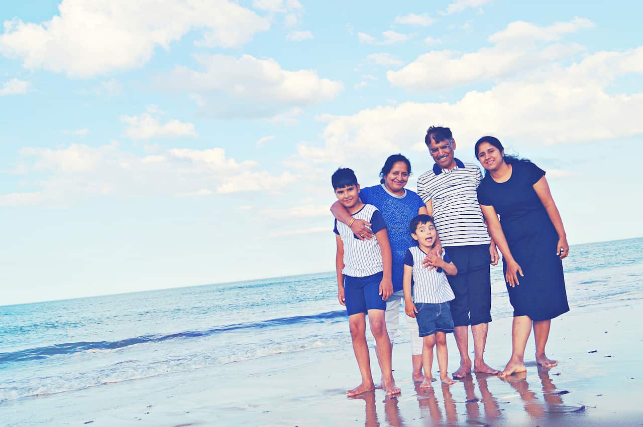 A family of five posing casually in a cheerful mood at a sandy beach