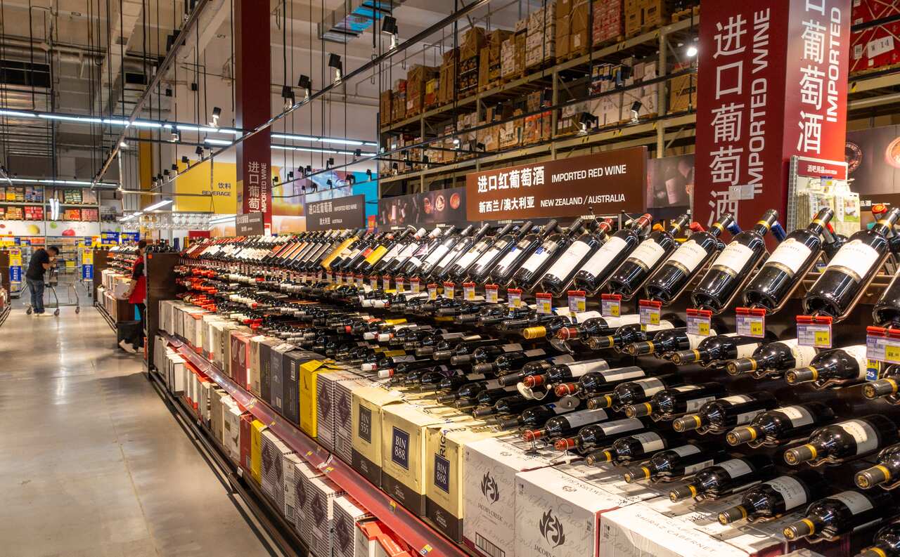 A supermarket aisle stacked with red wine bottles.