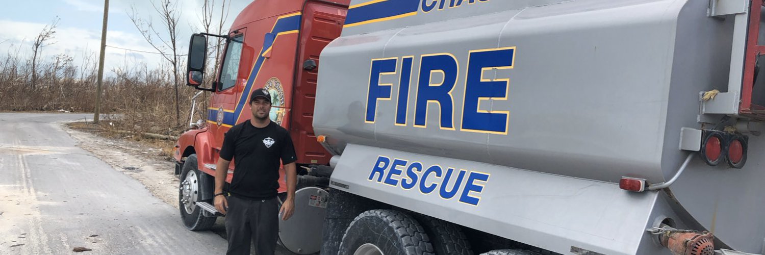 A man wearing a black T-shirt and cap stands next to a large truck marked “Fire Rescue”.