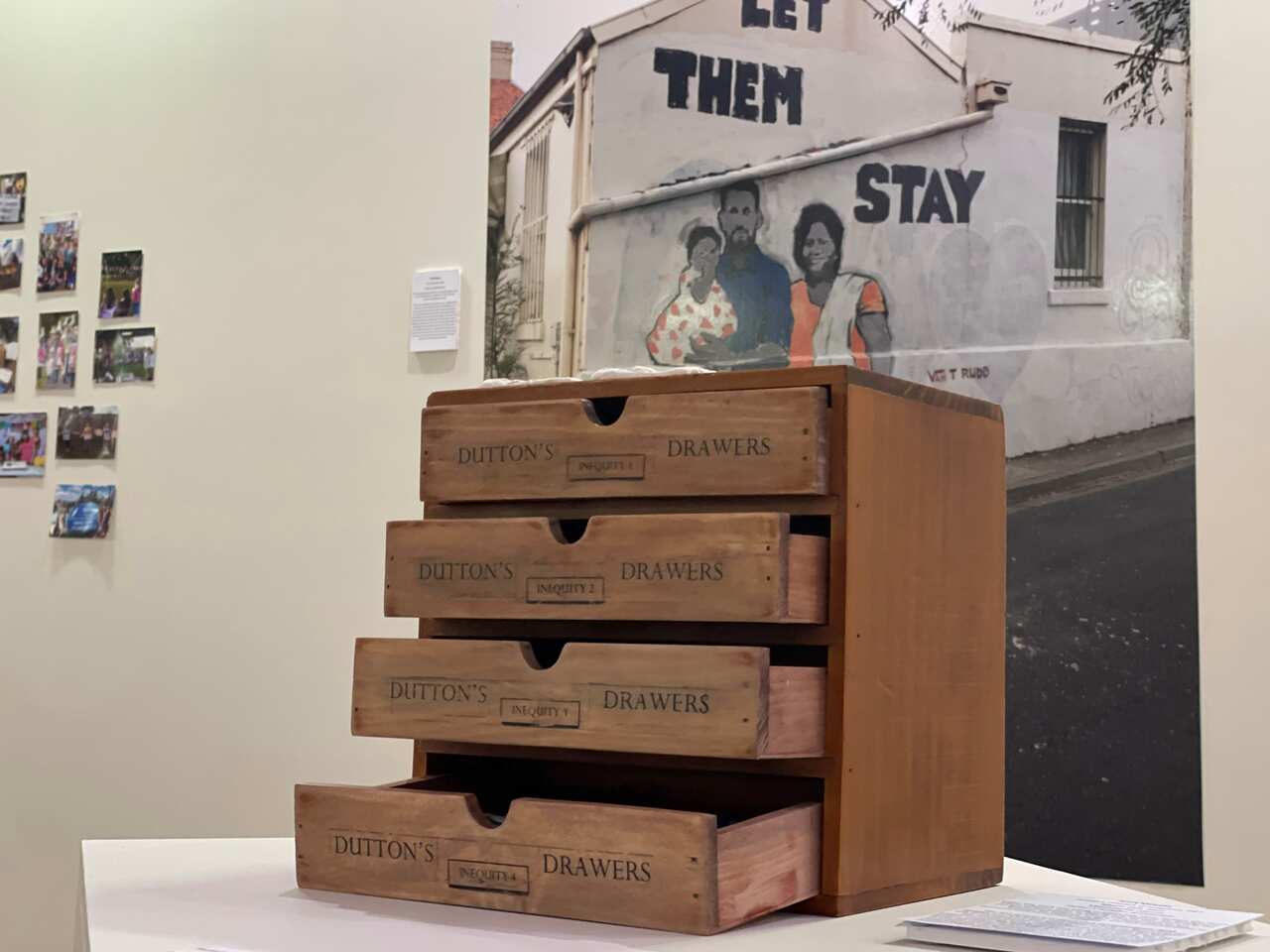 A wooden four-set drawer chest is opened, with each drawer saying "Dutton's Drawers". In the background is a mural of the family with the words, "let them stay". 