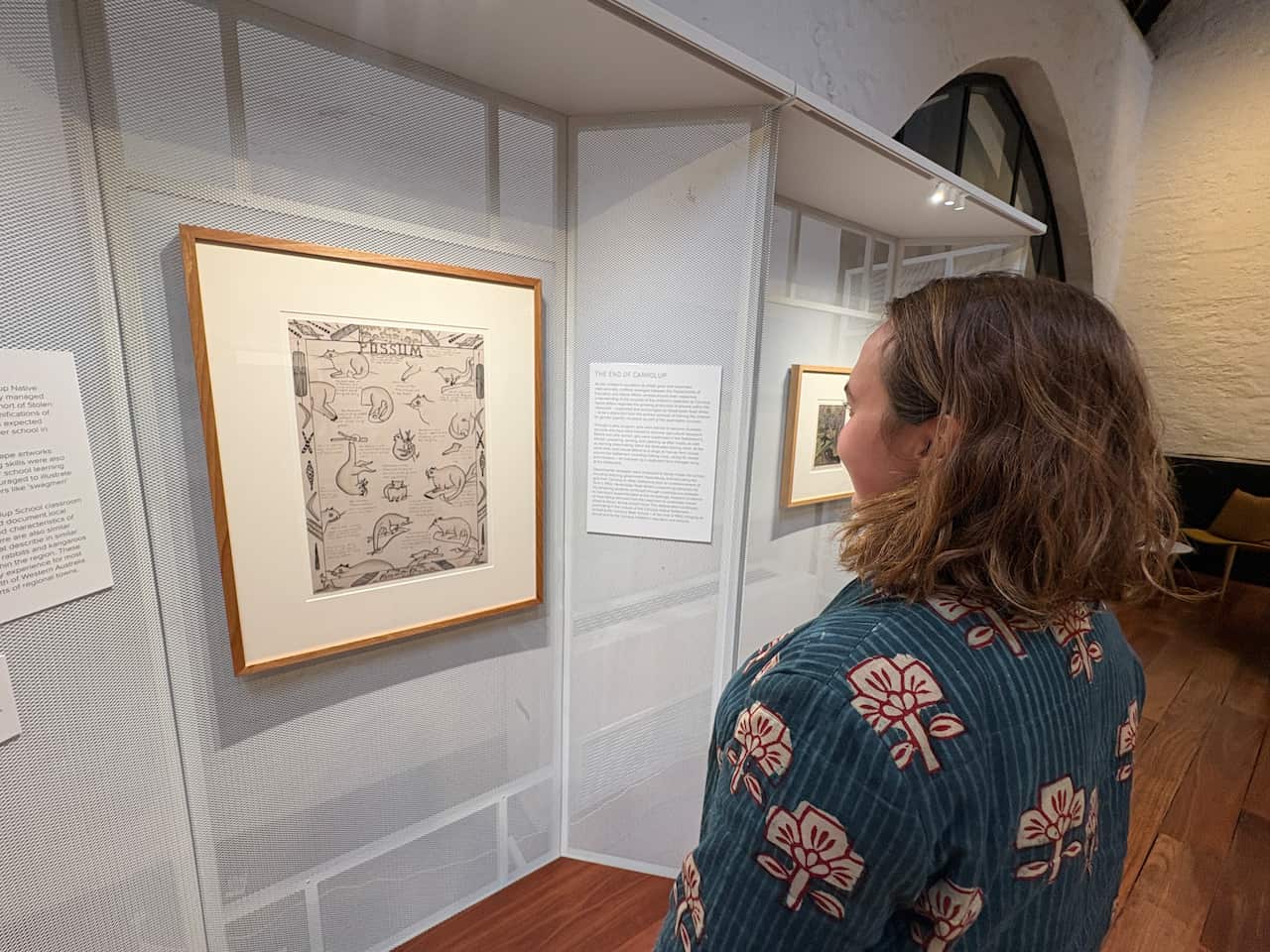 A woman looking at a framed illustration hanging in a gallery.