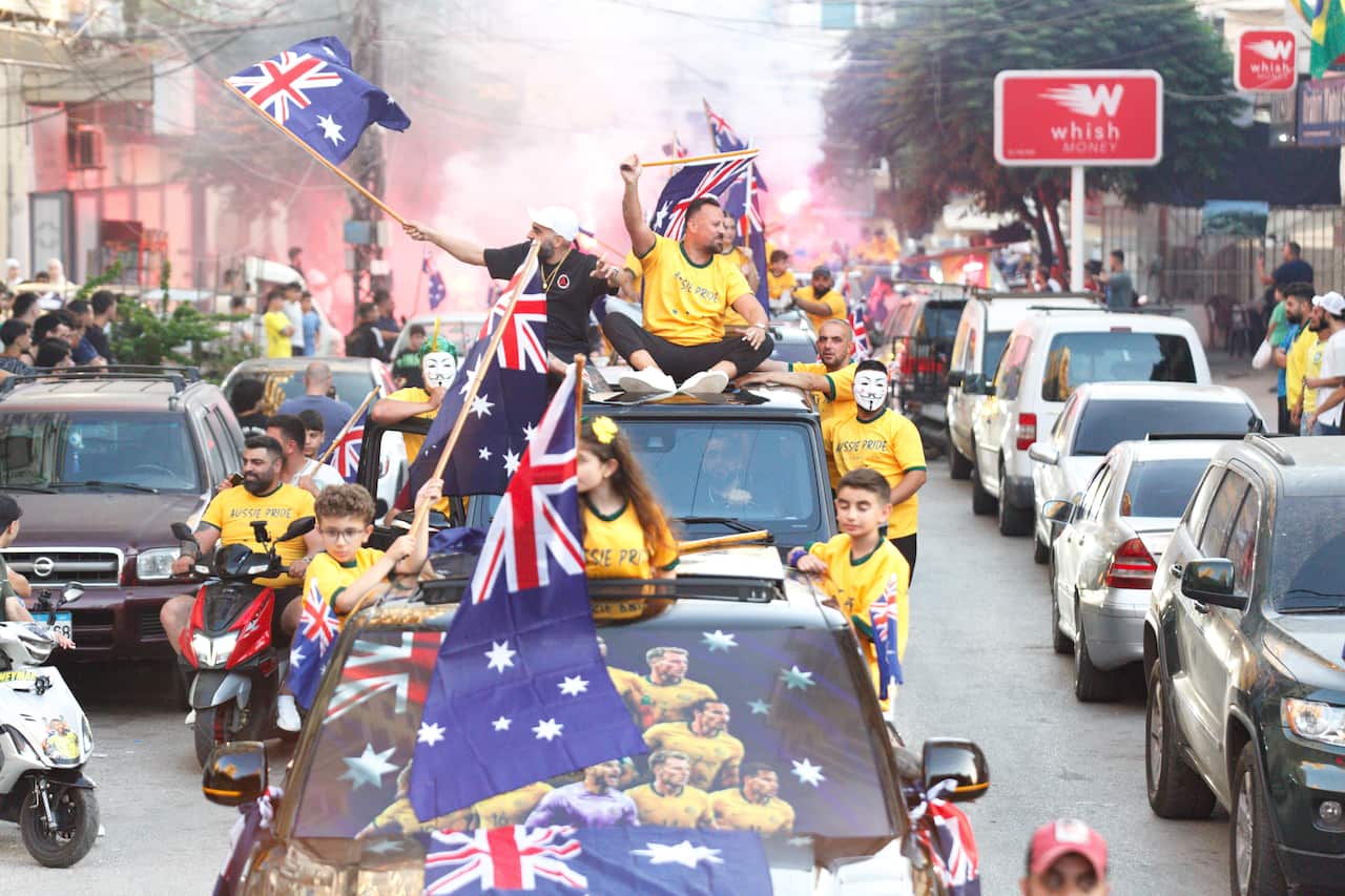 A motorcade of Australia supporters with children waving flags, while people let off flares in the background