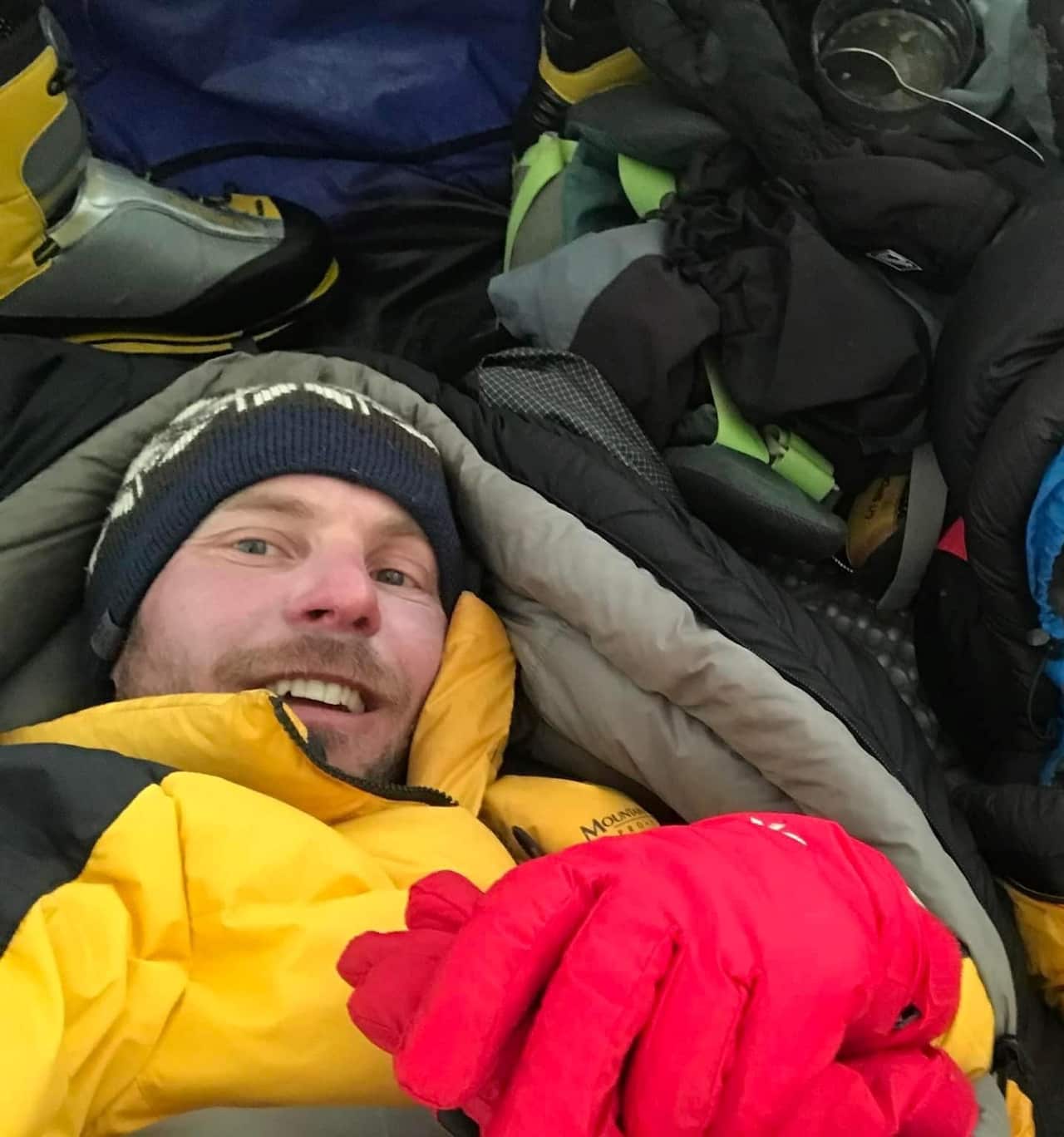 A man smiling while wearing many layers in a sleeping bag