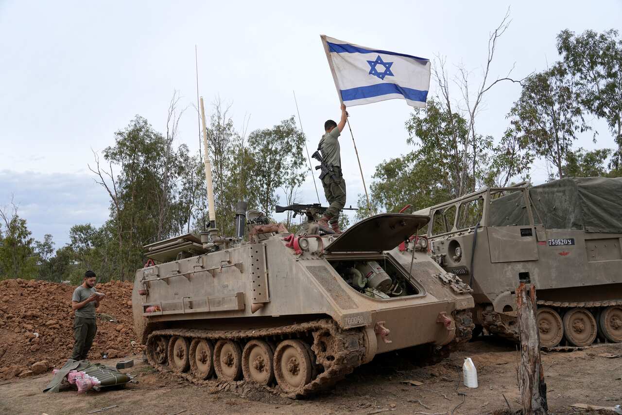 A Israeli soldier standing on top of a tank while another soldier stands next to it.