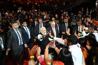 Anthony Albanese (right) and Narendra Modi stand among a large crowd, with attendees reaching out to shake Modi's hand, as both leaders are flanked by security personnel.