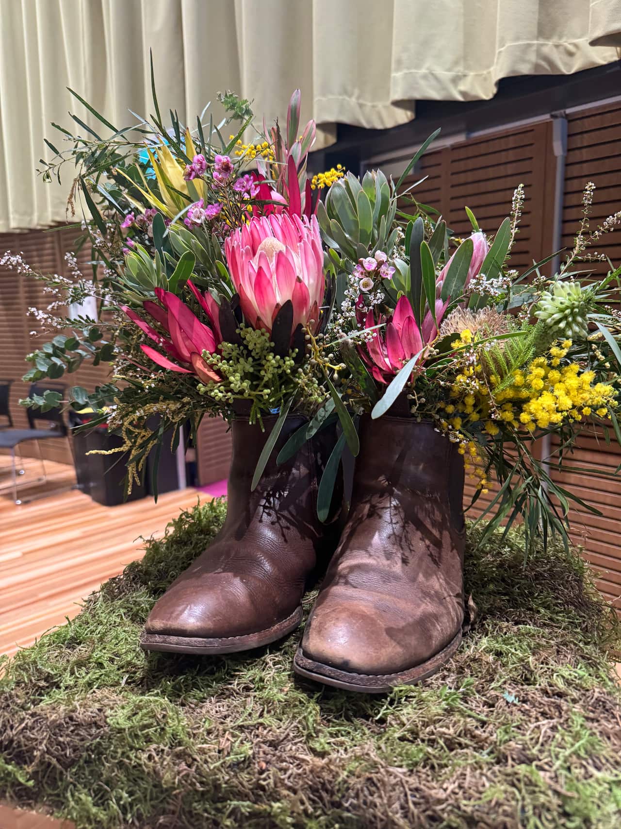 A pair of brown shoes holding bunches of flowers sitting on a patch of grass at a funeral.
