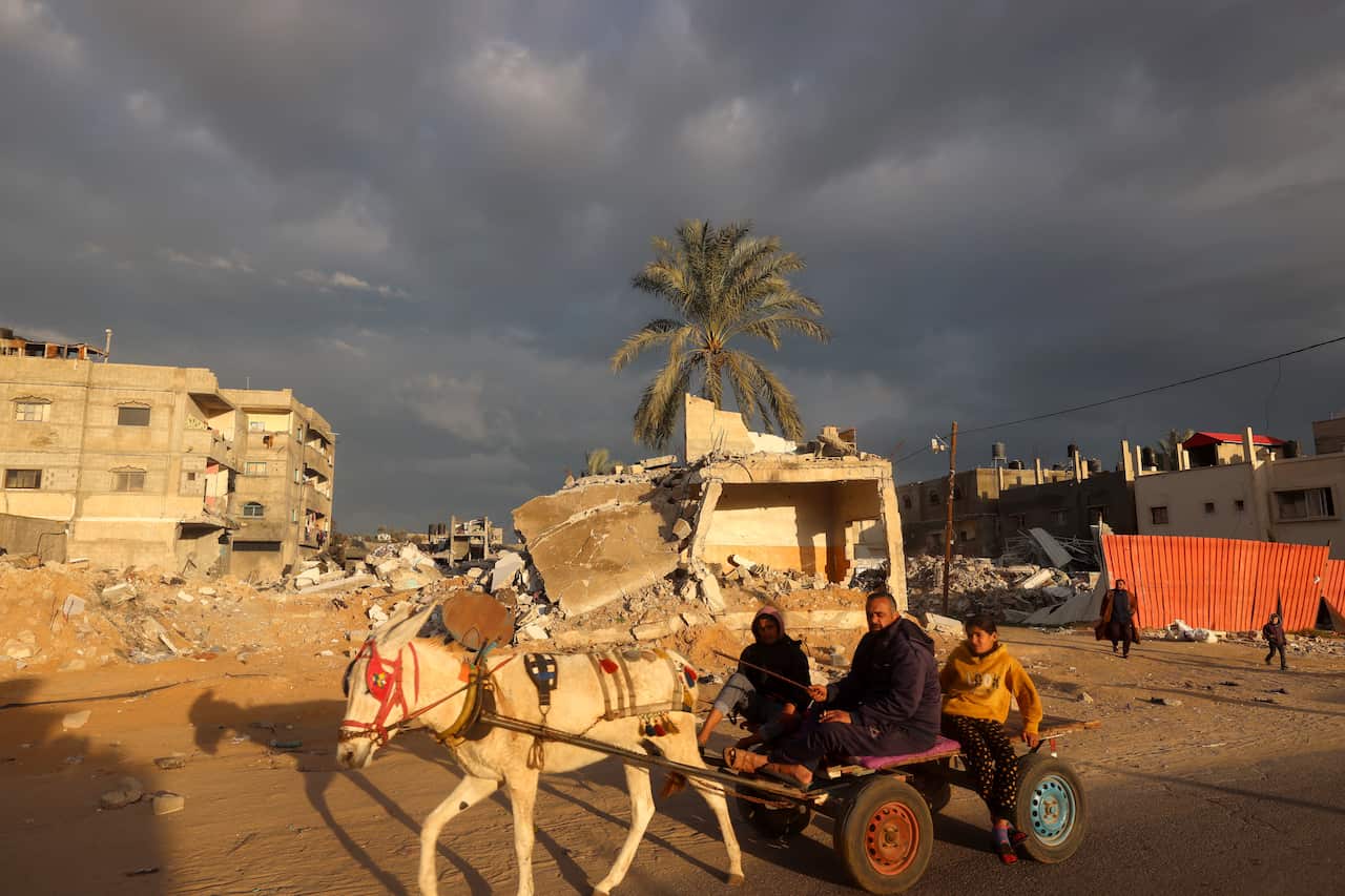 A Palestinian man rides a donkey-pulled cart near destroyed buildings.