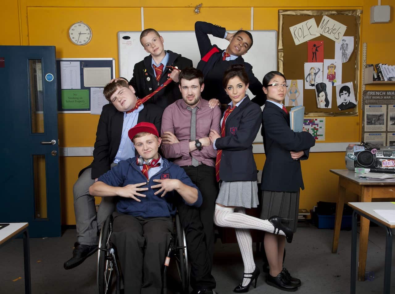 A young male teacher in a crumpled shirt and tie stands surrounded by five teenagers in school uniform also standing and a student in a wheelchair.jpg