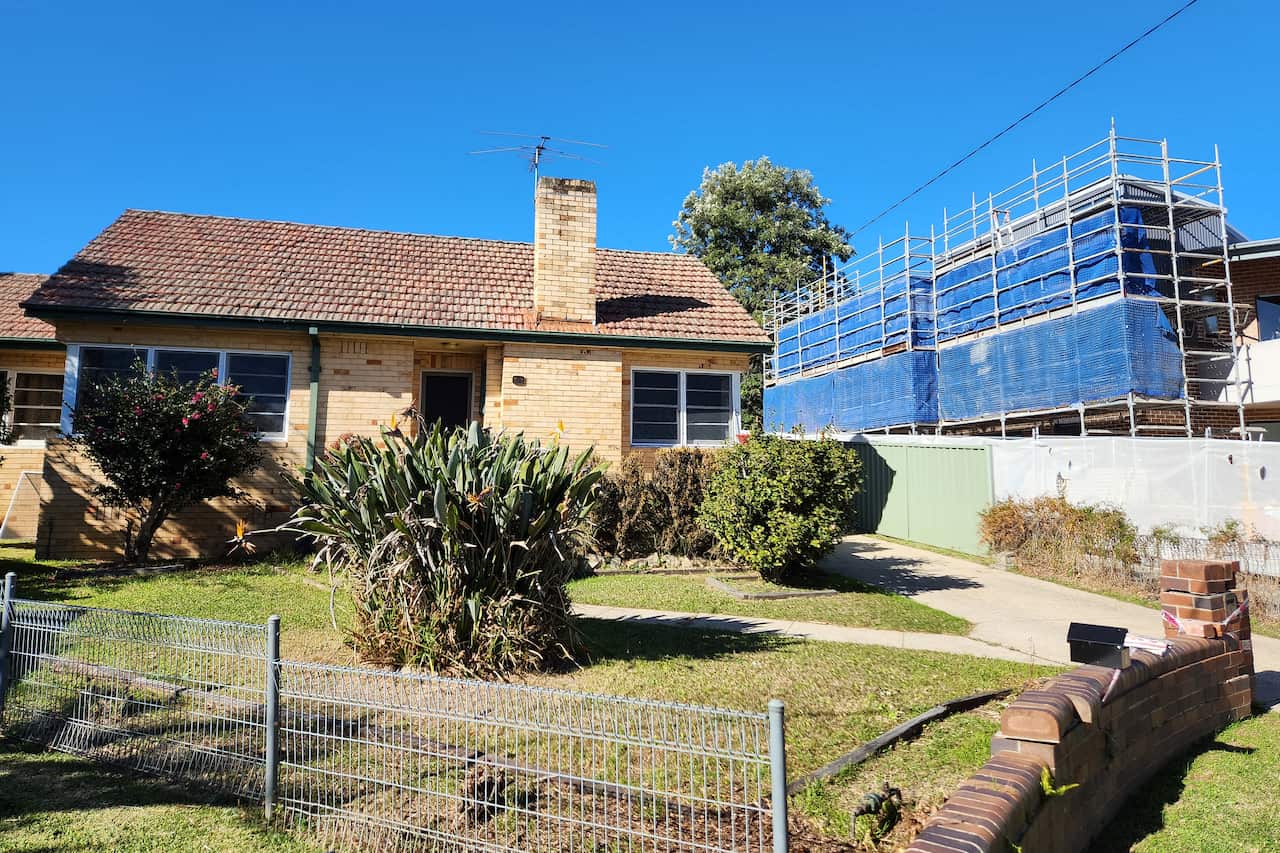 A brick home in front of a development project for a two-storey unit block in Westmead in western Sydney