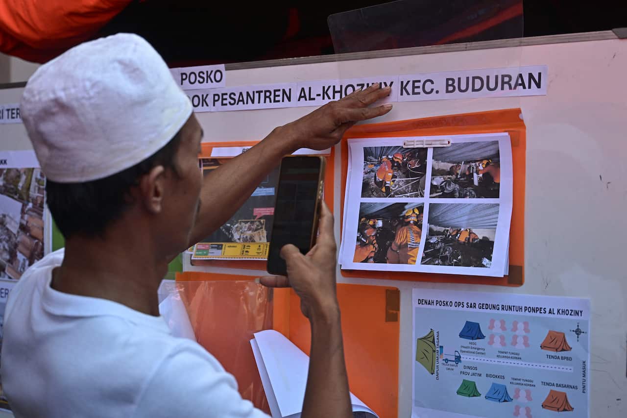 A relative of a student looks at pictures hung on a board as search and rescue operations continue 