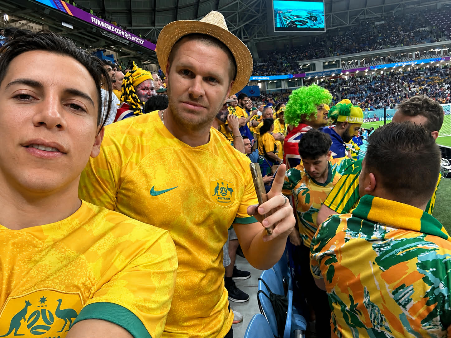Two men wearing gold Socceroos shirts at a football game