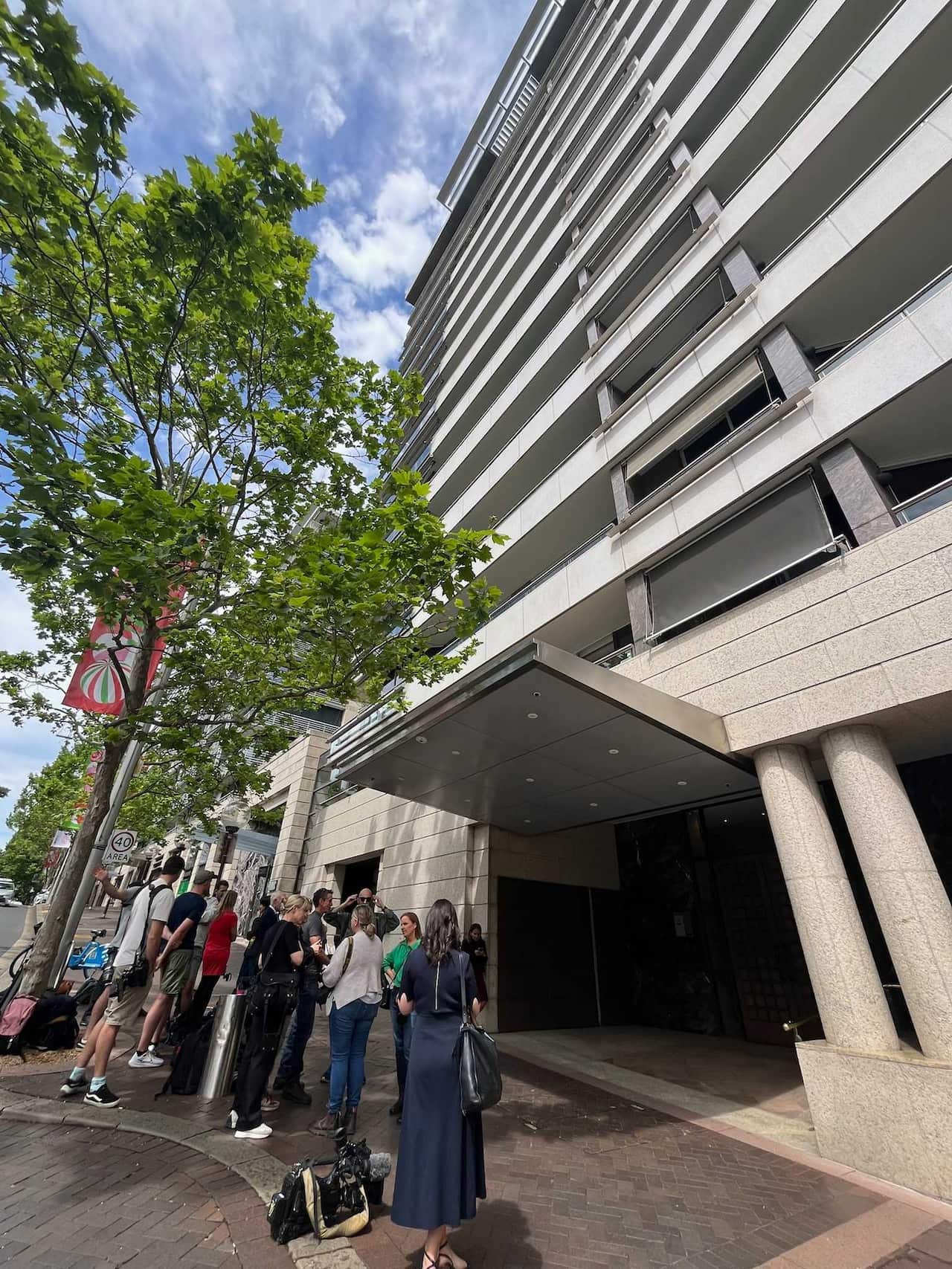 Media persons standing outside an apartment building.