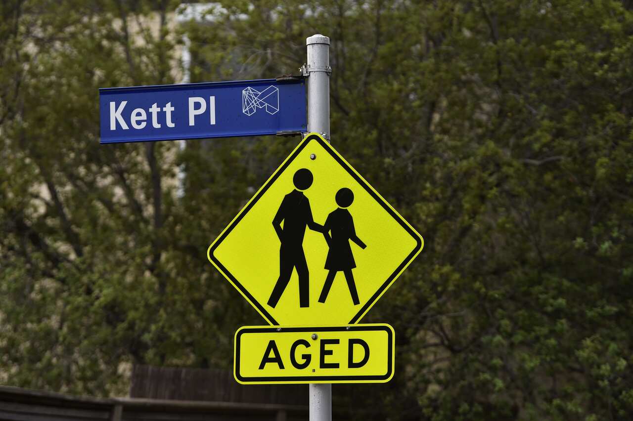 A blue street sign reading Kett Pl. Below it is a yellow and black sign featuring two people and below it the word aged.