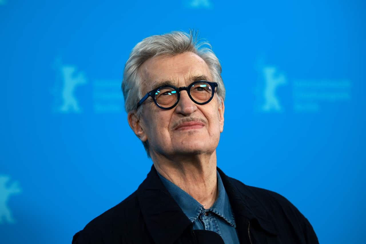 Wim Wenders standing in front of a blue background.