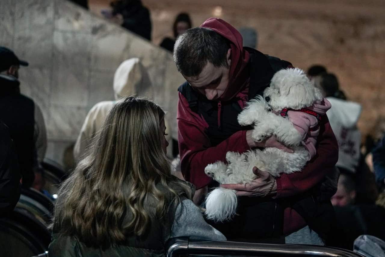 A man holding a white dog in a crowded underground metro.