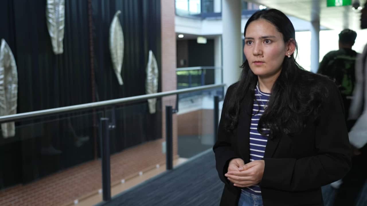 A young woman with dark hair and wearing a dark suit jacket looks to her right.