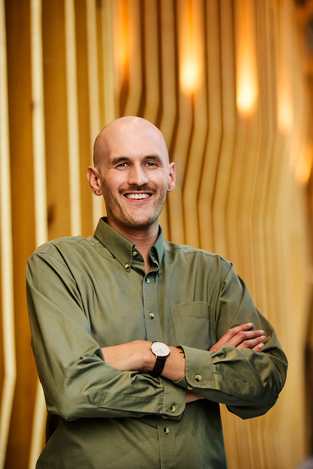 A bald man with a green shirt is smiling with his arms crossed 
