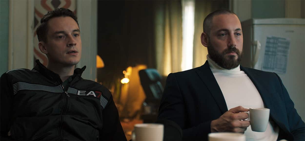 Two men sit at a kitchen table looking fierce.jpg
