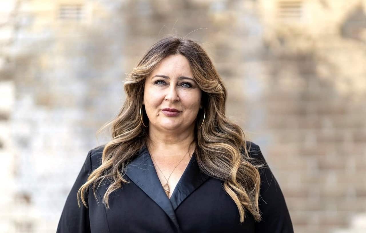 A woman wearing a black blazer looking into a camera.