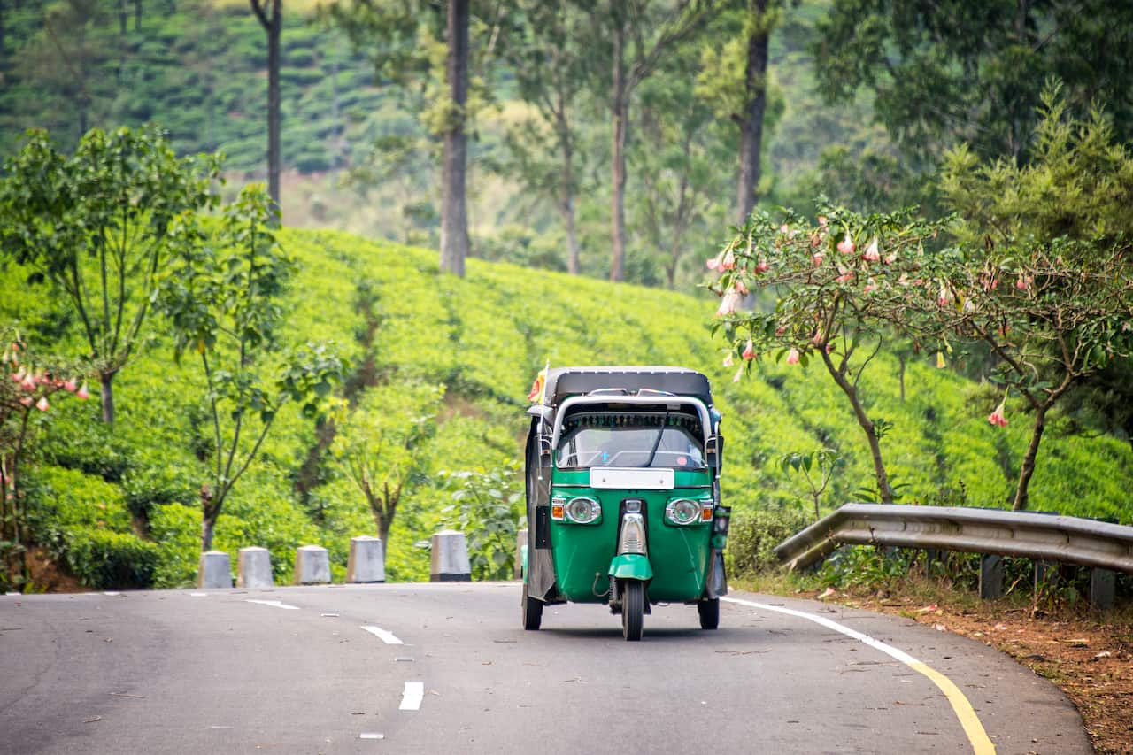 A tuktuk travelling a long a hilly road in Sri Lanka with tea plantations in the background.