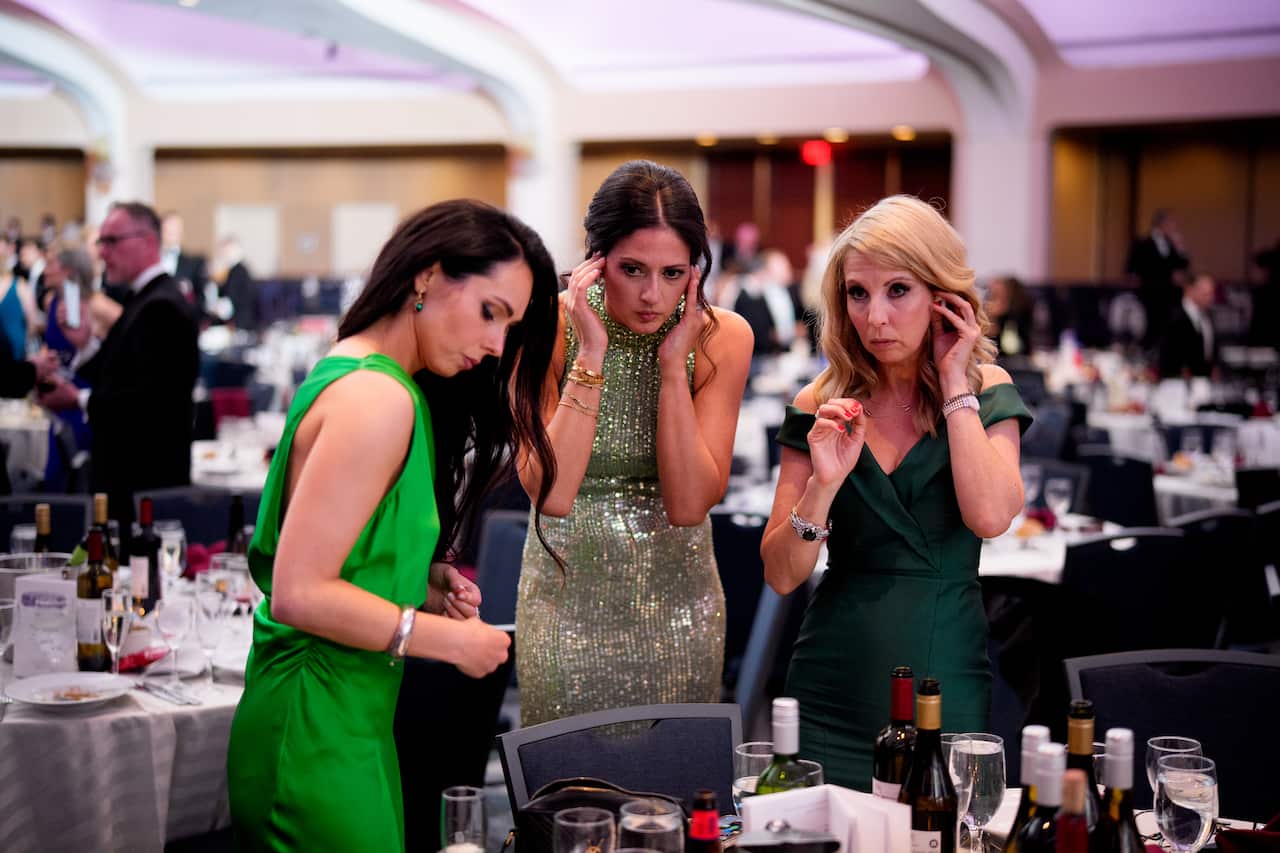 Three women standing in a ballroom next to a table.