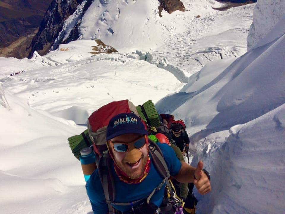 Matthew smiles, raising a thumbs up while backpacking on a snowy mountain 