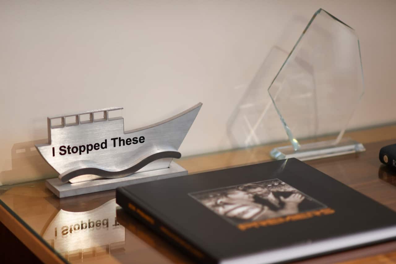 A metal block shaped as a boat carrying the words 'I stopped these' sits on a desk