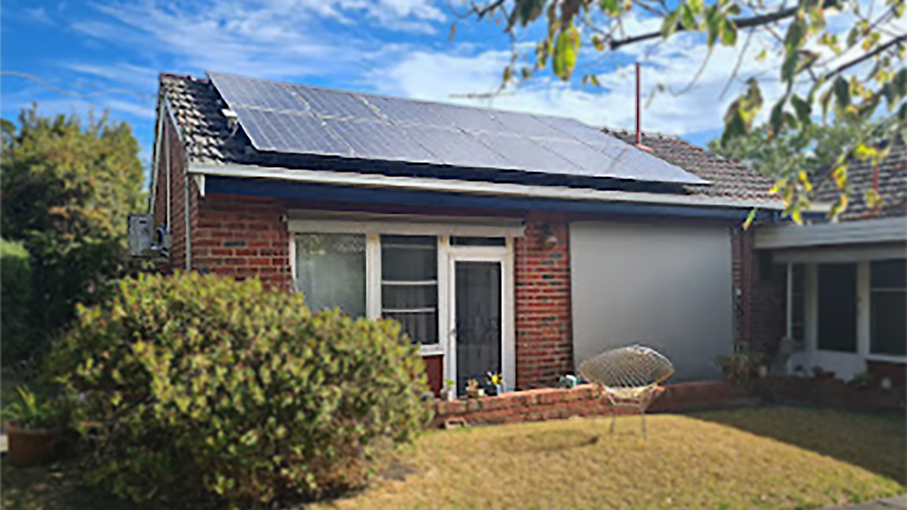the exterior of a small brick house with a lawn and bushes. There are solar panels on the roof