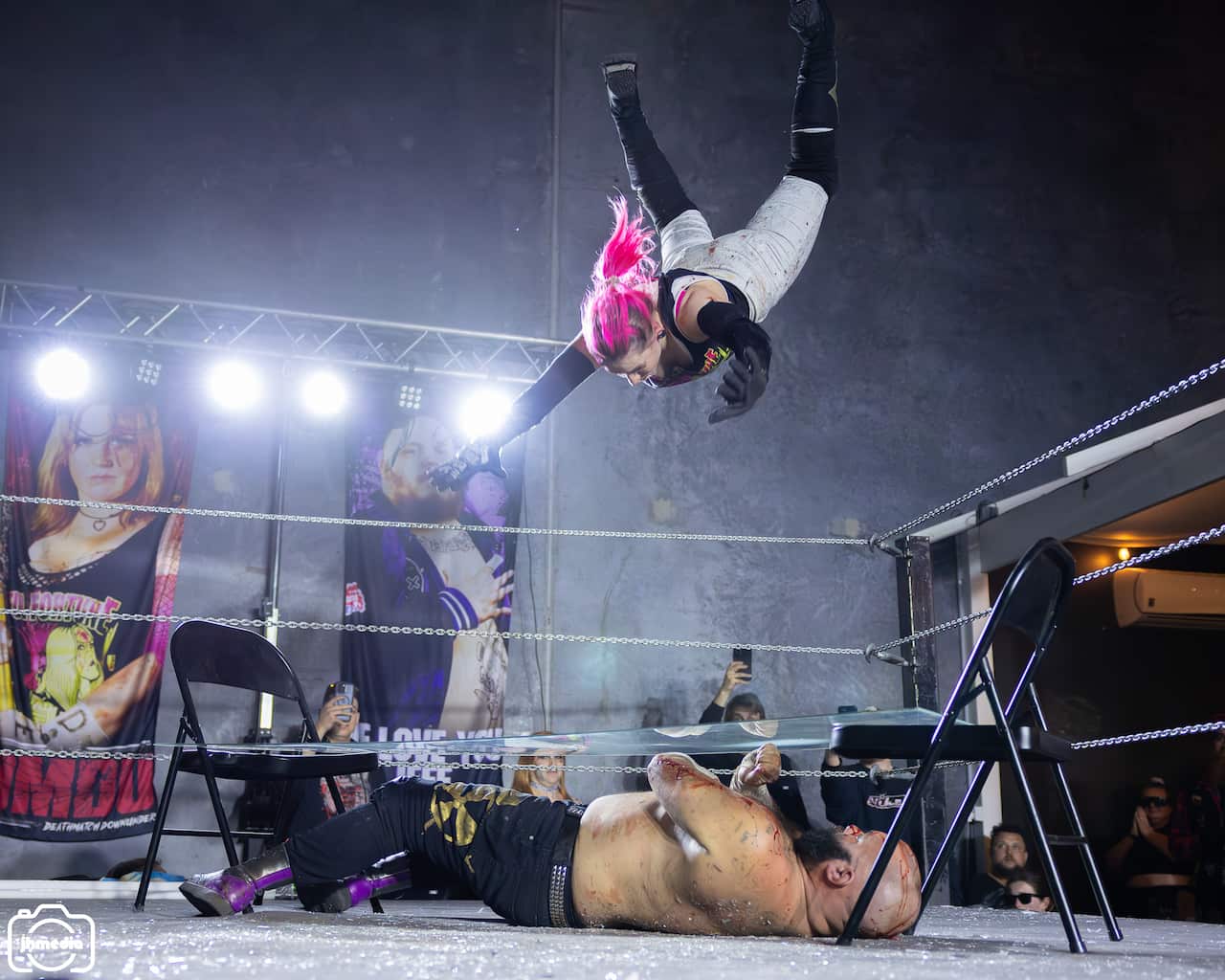 A person jumping off wrestling ropes into someone underneath a glass pane inside a wrestling ring. 