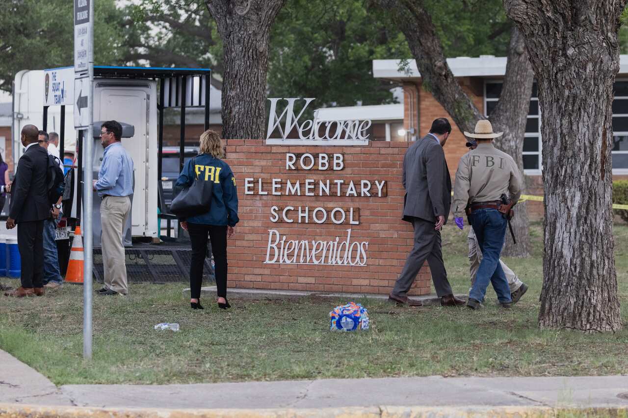 People walk near a small brick wall carrying the words: 'Welcome Robb Elementary School Bienvenidos 