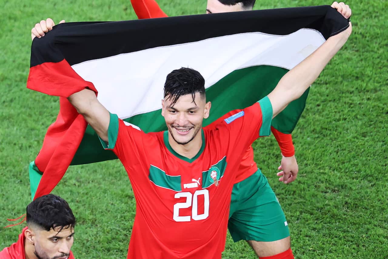 Man in red and green jersey carries Palestinian flag.