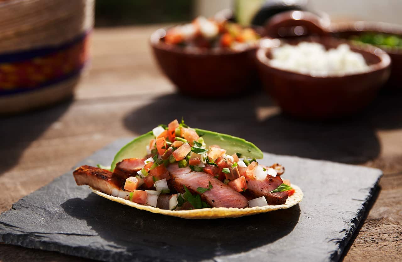 A flat tortilla holds meat, salsa and a slice of avocado. 