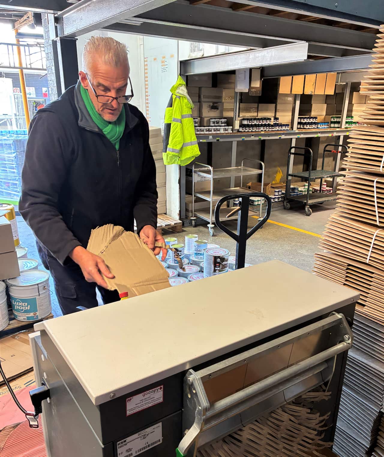 A man in a grey sweater feeds a cardboard panel into a machine. 