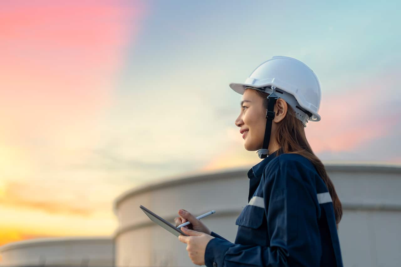 A woman wearning a hardhat writes on a clipboard