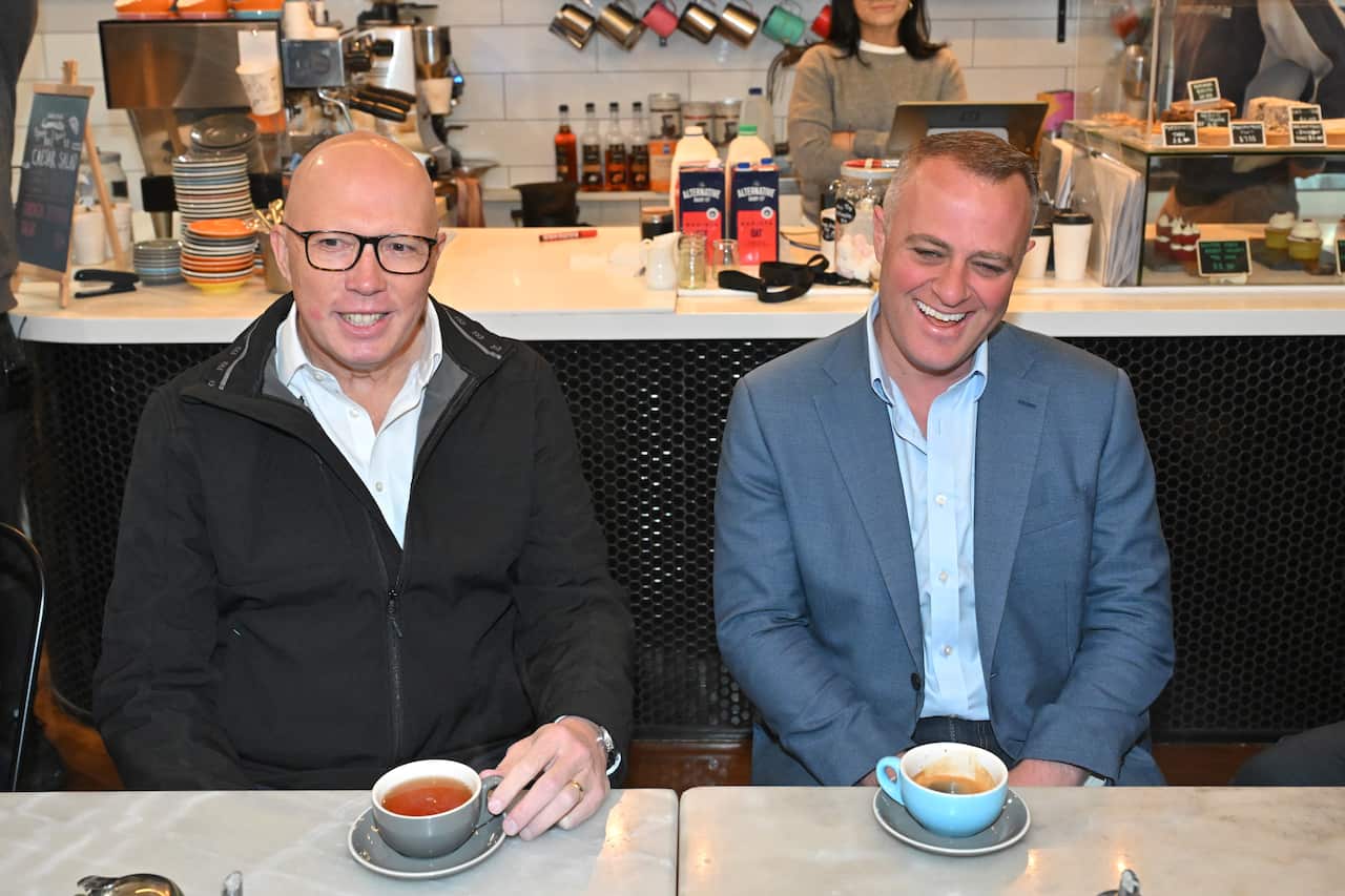 Two men sit at a table drinking coffees 