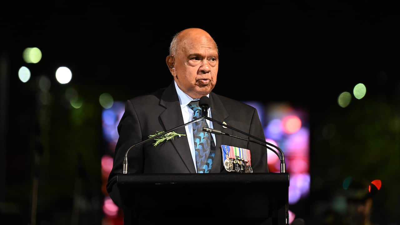 A man in a black blazer adorned with military badges is speaking at a podium.